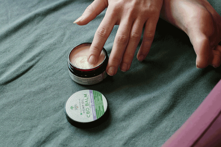 image of a woman's hand with her finger getting cannabis balm out of a container